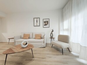 Ein modernes Wohnzimmer mit einer Couch, Sesseln, einem Couchtisch und zwei gerahmten Kunstwerken an der Wand.