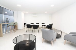 Una sala de reuniones moderna con separador de vidrio, sillas negras y grises, una mesa redonda de vidrio y un escritorio de madera con sillas.