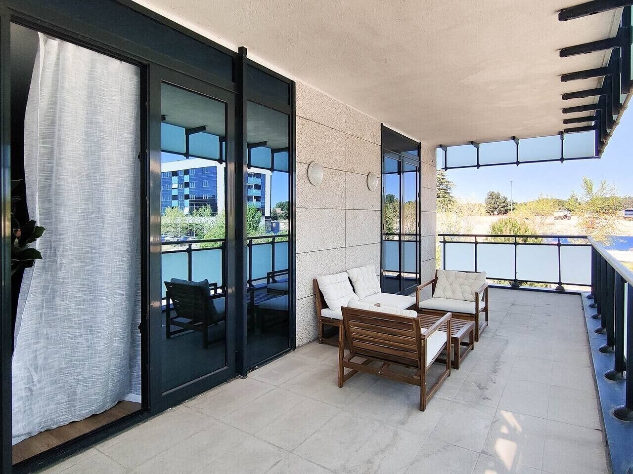 A balcony with a seating area, glass doors, and a view of buildings.