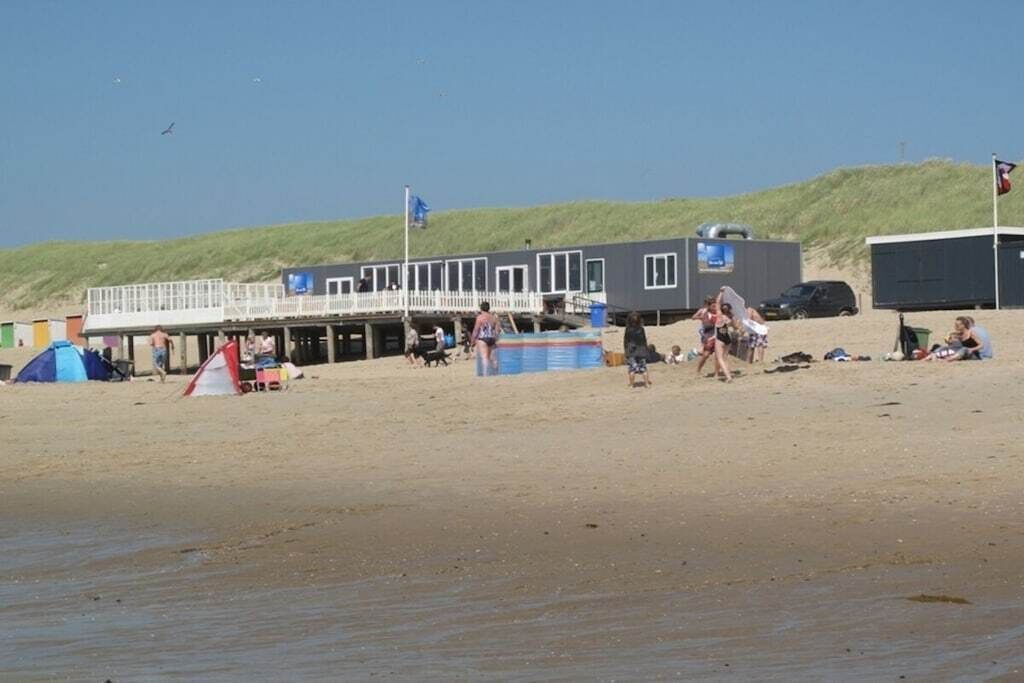 A beachside building with a deck, a blue tent, and people on the sand.