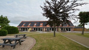 A building with a sloped roof, outdoor seating area, and a tree in the foreground. - Holiday apartment with 1 bedroom (Serooskerke)