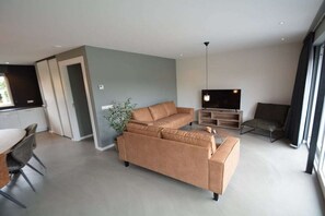 A modern living room with a sofa, a TV, and a dining area. - Holiday apartment with 1 bedroom (Serooskerke)