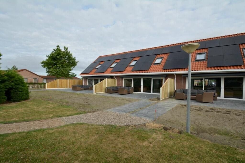 Un immeuble résidentiel doté d’un toit en pente, de grandes fenêtres et d’un espace extérieur aménagé pour s’asseoir.