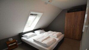A bedroom with a bed, a window, a wardrobe, and a small bedside table. - Holiday apartment with 1 bedroom (Serooskerke)