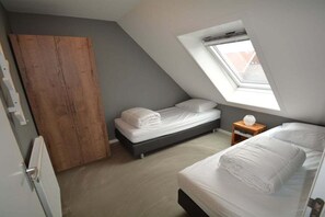 Ein Schlafzimmer mit zwei Betten, einem Holzschrank, einem kleinen Nachttisch und einem Oberlicht.