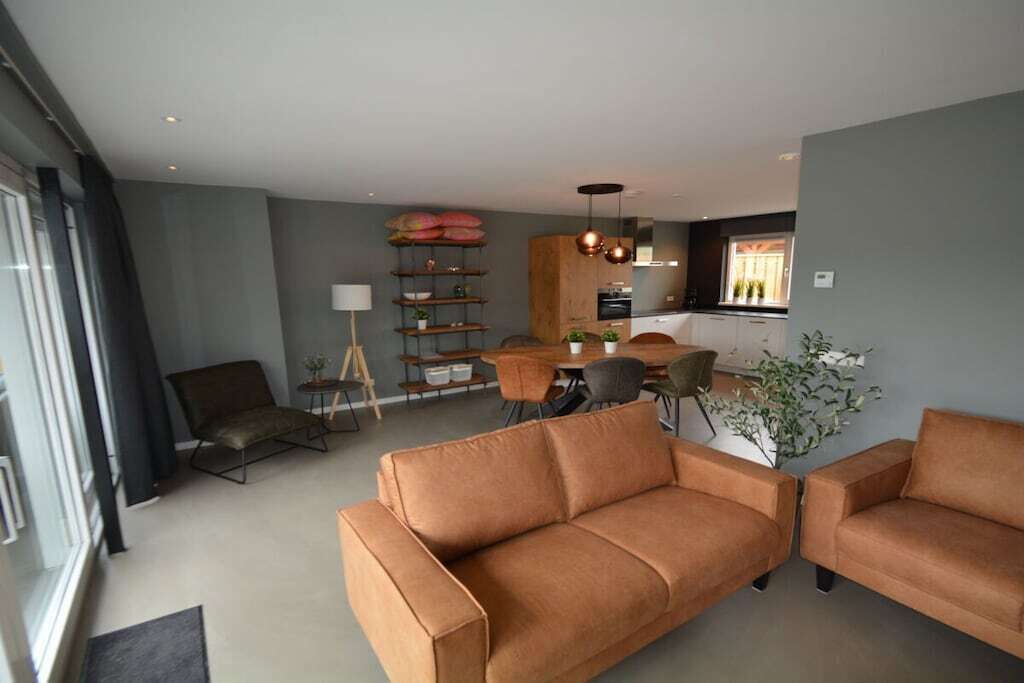 Ein modernes Wohnzimmer mit einer Couch, einem Essbereich mit Tisch und Stühlen und einer Küche im Hintergrund.