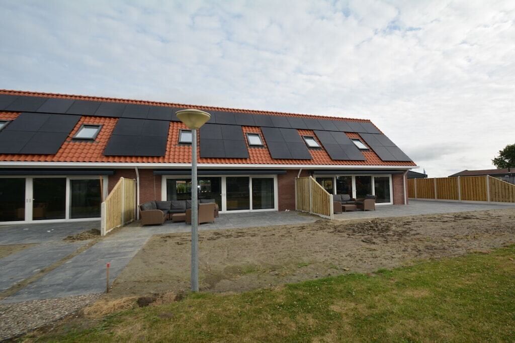 Una casa moderna con techo de tejas rojas, paneles solares y un porche cubierto.