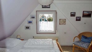 Une chambre à coucher comprenant un lit, une chaise, une fenêtre donnant sur une maison et des tableaux accrochés au mur.