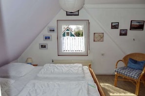 Ein Schlafzimmer mit einem Bett, einem Sessel, einem Fenster mit Blick auf ein Haus und Bildern an der Wand.