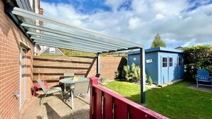 Une terrasse avec une table et des chaises, un abri de jardin bleu et une clôture en bois.