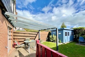 Eine Terrasse mit Tisch und Stühlen, ein blauer Schuppen und ein Holzzaun.
