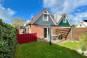 Ein zweistöckiges Haus mit geneigtem Dach, einem sichtbaren Schornstein und einem roten Zaun.