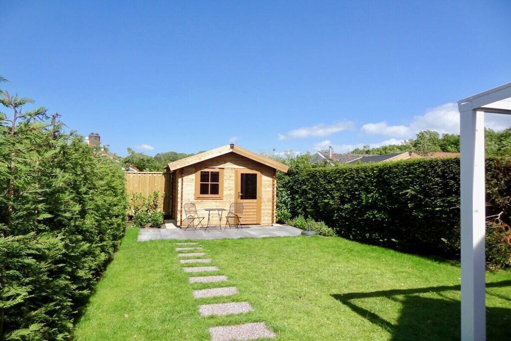 Una cabaña de madera con un pequeño patio, rodeada de un césped cuidado y un seto.