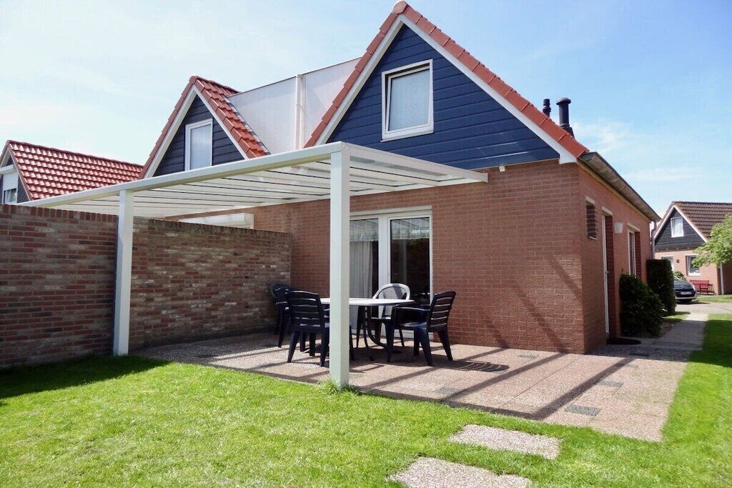 A residential house with a brick exterior, a white pergola, and a patio with a table and chairs.