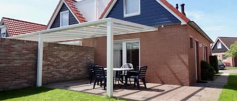 A residential house with a brick exterior, a white pergola, and a patio with a table and chairs.