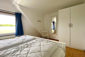 Ein Schlafzimmer mit Bett, einem Fenster mit Vorhängen, einem Sessel und einem Kleiderschrank.