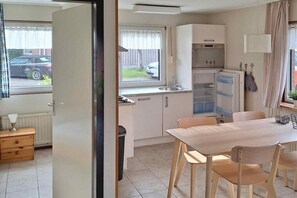 Eine kompakte Küche mit Kühlschrank, Backofen und Spüle. Es gibt einen Esstisch mit Stühlen und ein Fenster mit Jalousien.
