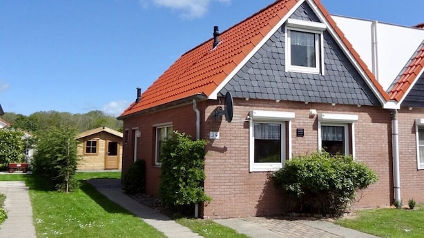 En toetages boligbygning med rødt tegltag, en synlig skorsten og en lille tilhørende garage.