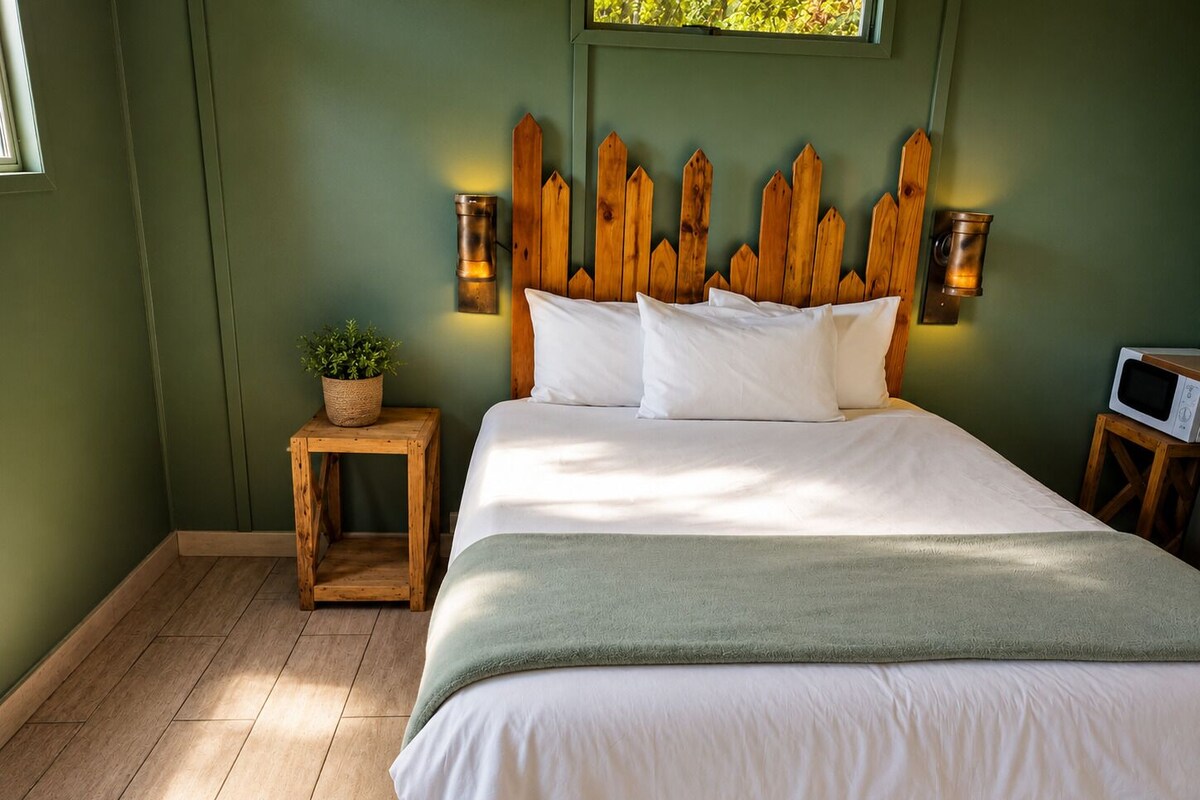 A bedroom with a bed, wooden headboard, bedside lamps, a small table with a plant, and a microwave.