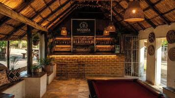 Zona de bar con techo de paja, mostrador de madera y mesa de billar.