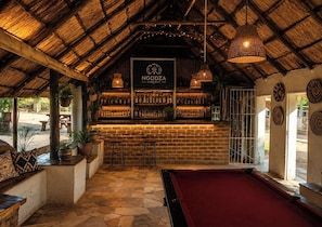 A bar area with a thatched roof, wooden bar counter, and a pool table. - Pagomo Lodges (Harare)