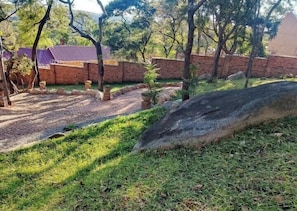 A paved pathway leading to a brick wall, surrounded by grass and trees.
