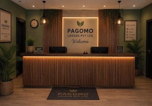 A reception desk with a sign reading 'Pagomo Lodges Pvt Ltd Welcome' and a 24/7 reception sign.