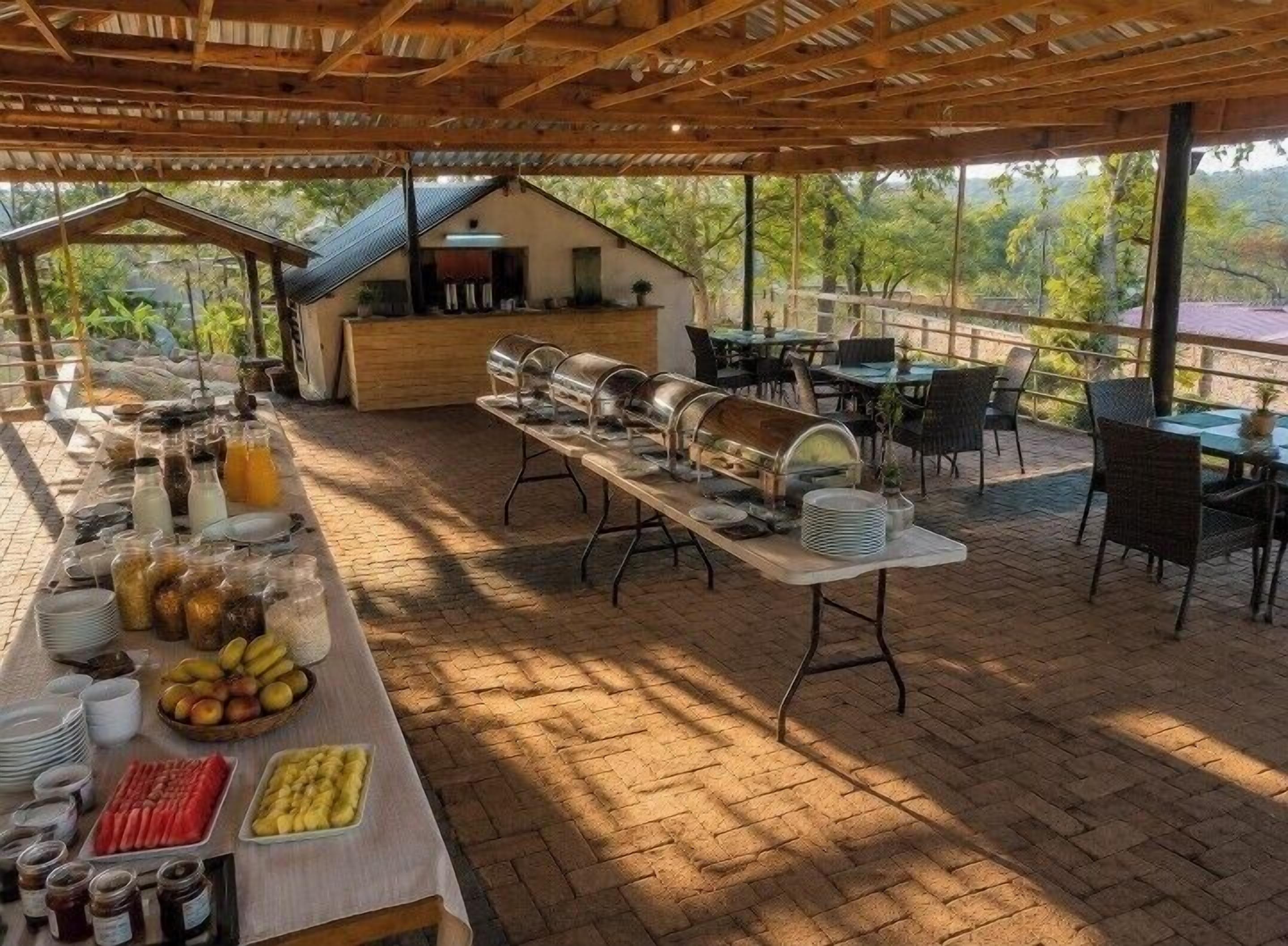 Un área de comedor al aire libre con mesas y sillas, una barra de buffet y vistas del paisaje circundante.