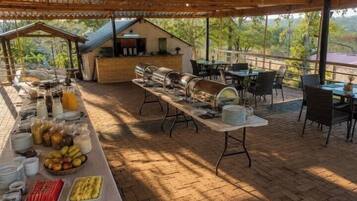 Un área de comedor al aire libre con mesas y sillas, una barra de buffet y vistas del paisaje circundante.