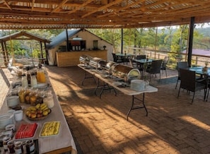 An outdoor dining area with tables and chairs, a buffet setup, and a view of the surrounding landscape. - Pagomo Lodges (Harare)