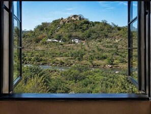 A view through a window of a hillside with a river and vegetation. - Pagomo Lodges (Harare)