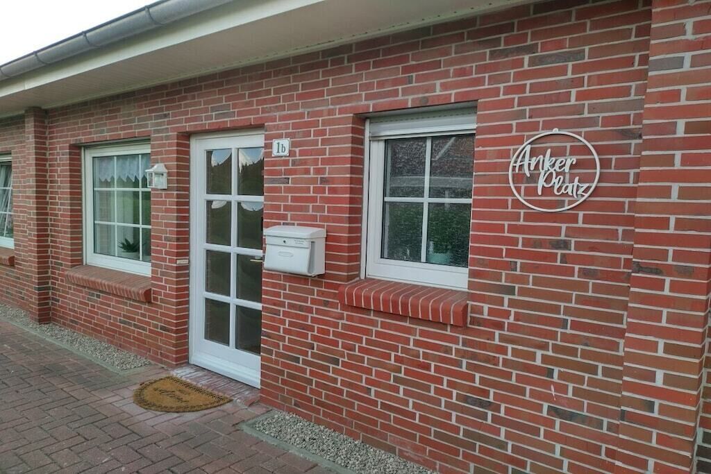 Un edificio de ladrillo rojo con puerta y ventanas blancas, un buzón y un letrero que dice 'Anker Platz'.