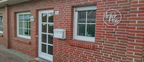 Un edificio de ladrillo rojo con puerta y ventanas blancas, un buzón y un letrero que dice 'Anker Platz'.