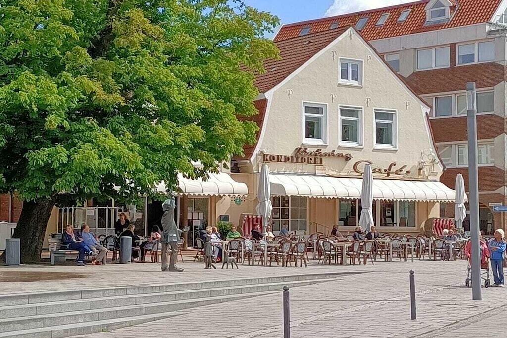A cafe with outdoor seating, a tree, and a building with a sign.