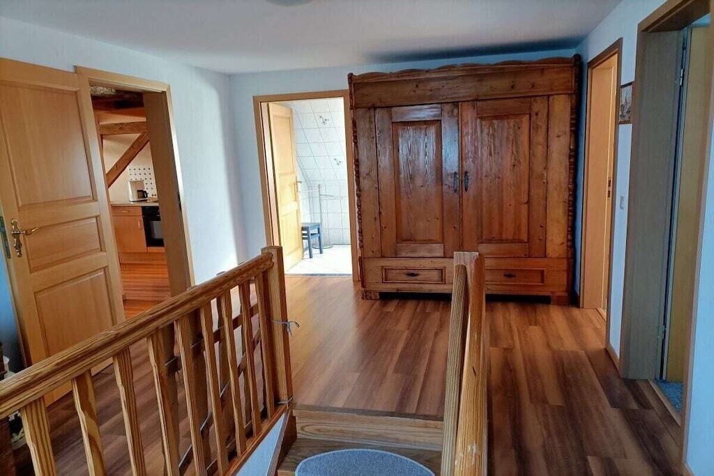 Una escalera de madera conduce a una habitación con un amplio armario de madera y vistas a una zona de cocina.
