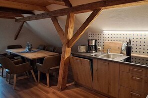 Eine Küche mit Holzbalken, einem Esstisch mit Stühlen, einer Kaffeemaschine und einem Spülbecken.