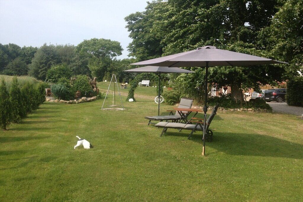 A grassy outdoor area with a swing set, picnic table, and umbrella.
