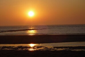 A sunset over a beach with the sun low on the horizon, reflecting on the water. - Holiday villa Windrose (JULIANADORP)