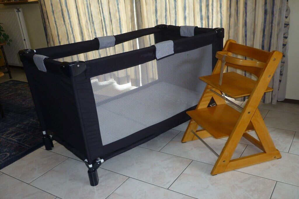 A baby playpen with a mesh side and a wooden chair.