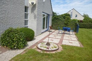 A house with a paved patio, a circular garden feature, and a blue table with chairs. - Holiday villa Windrose (JULIANADORP)