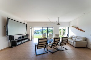 A spacious living room with a large flat-screen TV, a dining area with chairs, a sofa, and a view of the outdoors. - The Heli House | Private Pool, Movie Theater, Gym & Games (Viseu)