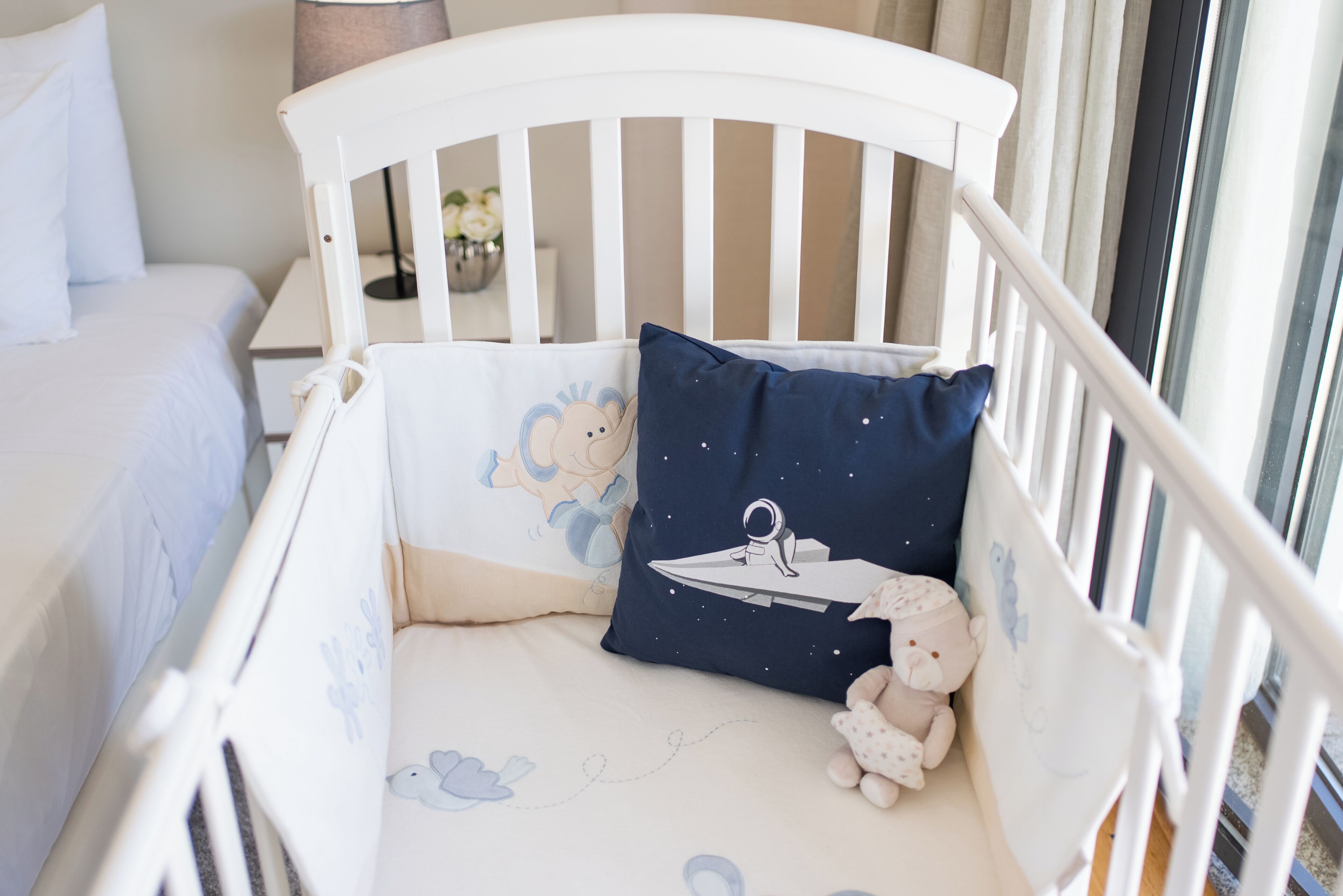 Berço branco com travesseiro azul com tema de astronauta e travesseiro branco com desenho de urso.
