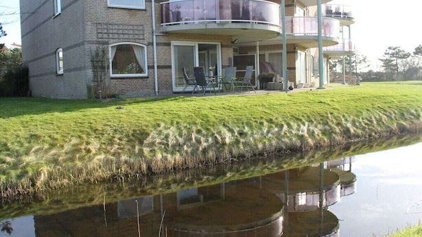 Um edifício residencial com vários andares, teto plano, janelas amplas e uma varanda com guarda-corpo de vidro.