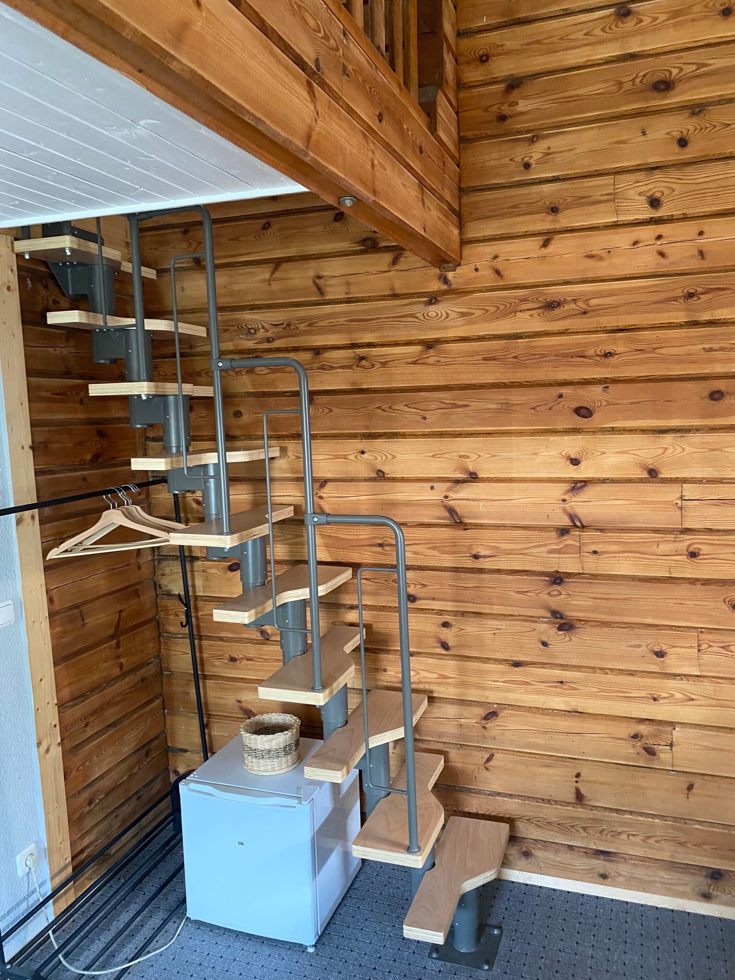 Interior de madera con una escalera de metal y un pequeño electrodoméstico blanco en el suelo.