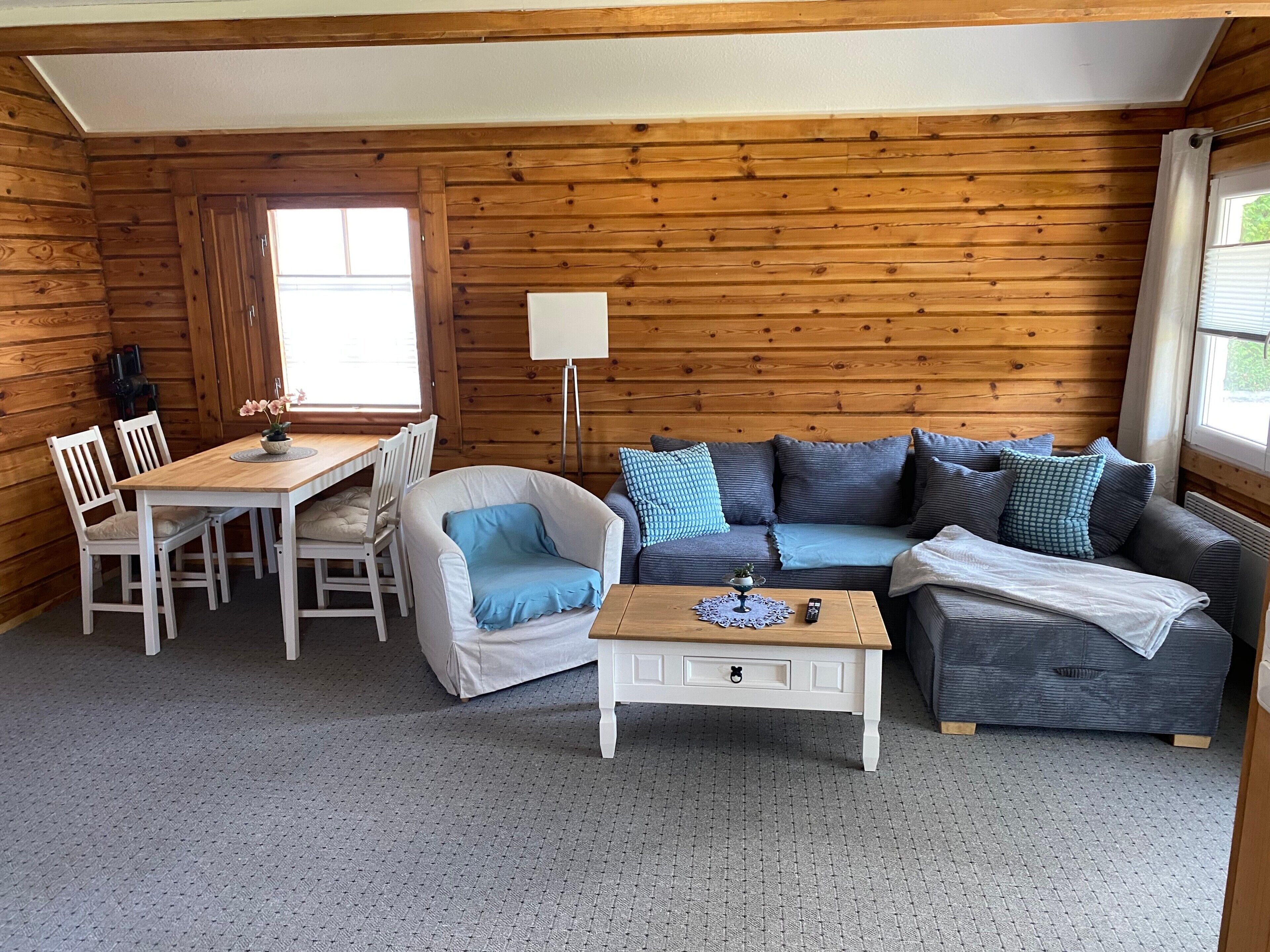 Ein Interieur einer Holzhütte mit einem Esstisch, zwei Stühlen, einer Couch, einem Couchtisch und einer Lampe.