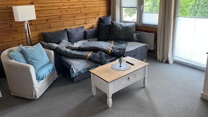 A cozy room with a wooden wall, a sofa, a chair, a small table, and a window with curtains.
