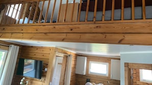 A wooden interior with a balcony, a television, and a window.