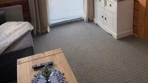Quarto com teto de madeira, televisão na parede, armário branco, cama com manta branca e janela com cortinas.