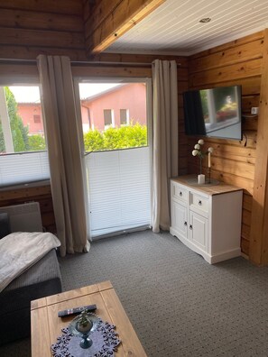 A room with a wooden ceiling, a television mounted on the wall, a white cabinet, a bed with a white blanket, and a window with curtains. - Holiday Home 'Haus Der Sinne' with Private Terrace and Wi-Fi (Wolgast)