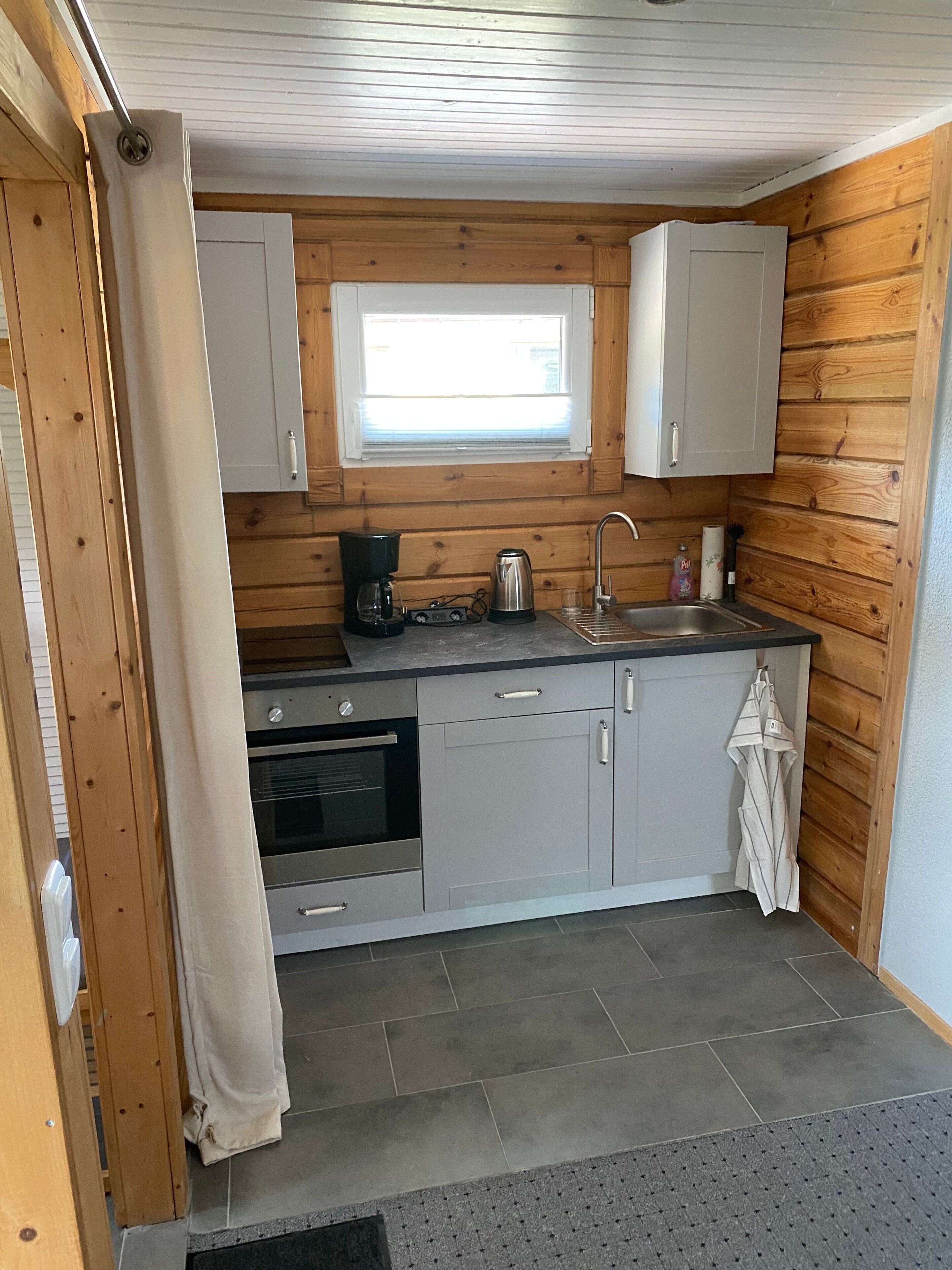 A compact kitchen with wooden walls, a window, a sink, and a stove.